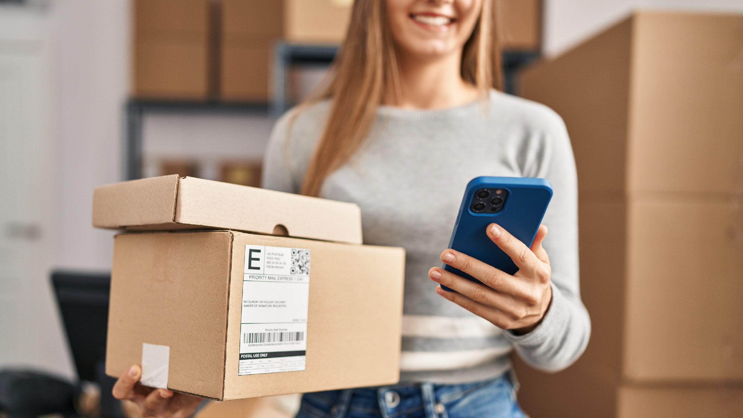 Vrolijke vrouw die pakketten balanceert in één hand en een mobiele telefoon vasthoudt in de andere